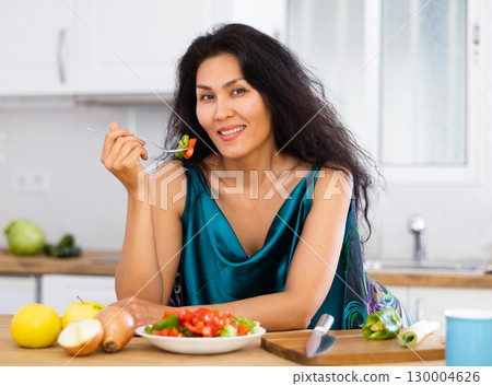 Portrait of positive woman in nightdress eating salad at home 130004626