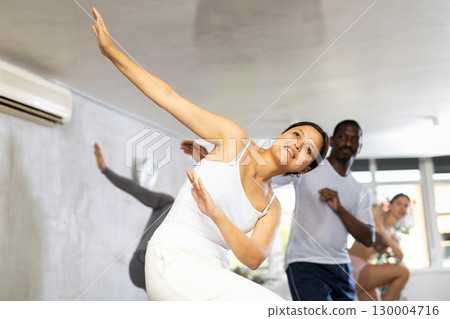 Group of happy sports woman and men in activewear exercising dynamic dancing movemens in gym studio 130004716