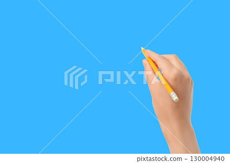 A hand holds a yellow pencil over a blue surface A hand holds a yellow pencil over a blue surface 130004940