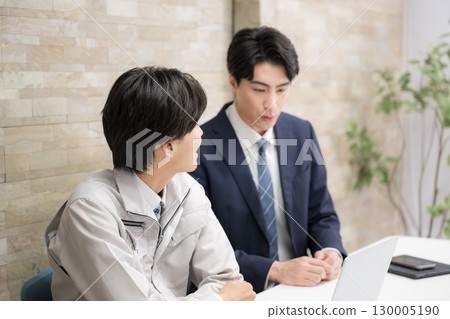A man in a suit and work clothes from a construction management company checking documents at a general contractor's site. He is seriously checking documents during a meeting. 130005190