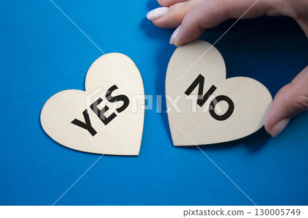 Yes or No symbol. Concept word Yes or No on wooden hearts. Businessman hand. Beautiful blue background. Business and Yes or No concept. Copy space Yes or No symbol. Concept word Yes or No on wooden hearts. Businessman hand. Beautiful blue background. Business and Yes or No concept. Copy space 130005749