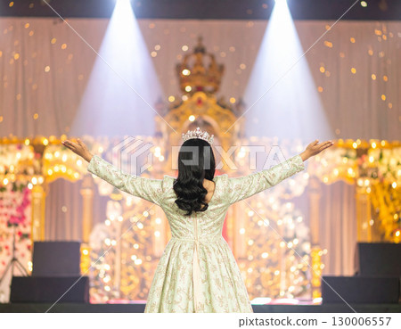 AI generated A radiant beauty queen stands at the frame edge gesturing toward a sparkling pageant stage with spotlights. The dazzling backdrop evokes elegance, competition and dream-come-true moments 130006557