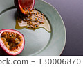 Half a passion fruit on a plate with fruit and juice spilling out 130006870
