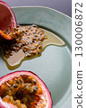 Half a passion fruit on a plate with fruit and juice spilling out 130006872