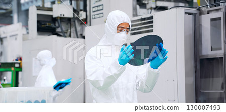 Male worker in protective clothing inspecting silicon wafers in a semiconductor factory Male worker in protective clothing inspecting silicon wafers in a semiconductor factory 130007493