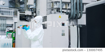 A female worker in a dust-proof suit inspecting silicon wafers in a semiconductor factory A female worker in a dust-proof suit inspecting silicon wafers in a semiconductor factory 130007495