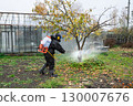man in mask and overalls sprays garden with against pests in autumn. 130007676