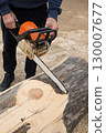 professional lumberjack saws logs, holding a chainsaw in his hand, to build wooden house. 130007677