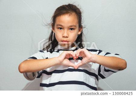 An Asian girl making a heart shape with her hands, symbolizing love, care, and friendship, standing against a plain background. An Asian girl making a heart shape with her hands, symbolizing love, care, and friendship, standing against a plain background. 130008425