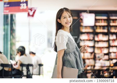 Smiling young woman standing in the library 130009718