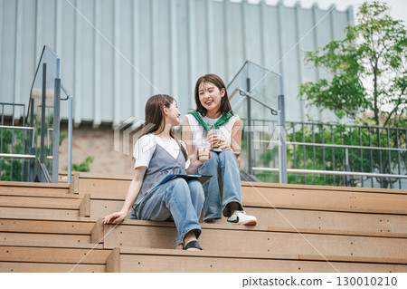Young woman sitting and talking with friends on outdoor stairs 130010210