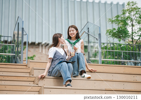 Young woman sitting and talking with friends on outdoor stairs 130010211