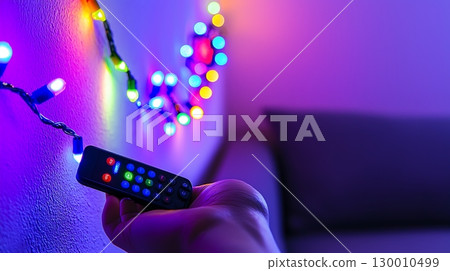 A person is holding a remote control in front of a wall with lights on it 130010499