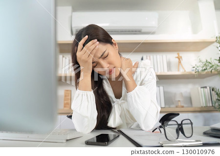 Mental Health. Woman experiencing headache while working at her desk. 130010976