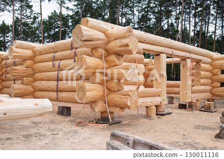 The construction site of a wooden house. Traditional log cabin built from wood logs on sunny summer day. The construction site of a wooden house. Traditional log cabin built from wood logs on sunny summer day. 130011116