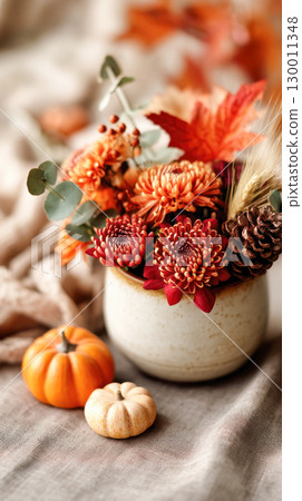 Autumn floral arrangement featuring vibrant orange flowers, decorative pumpkins, and natural elements creating a warm seasonal atmosphere 130011348