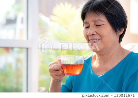 Senior asian woman enjoying drinking tea sitting on sofa with satisfied in living room at home. Senior asian woman enjoying drinking tea sitting on sofa with satisfied in living room at home. 130011671