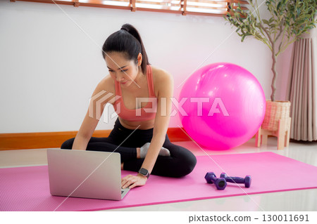 Young asian woman watch laptop for practice yoga and workout in living room at home. Young asian woman watch laptop for practice yoga and workout in living room at home. 130011691
