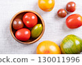 Fresh and ripe tomatoes of various varieties, colors, and sizes in a wooden bowl, on linen. Varieties of the plant Solanum lycopersicum, whose fruits are edible berries and are eaten as vegetables. 130011996