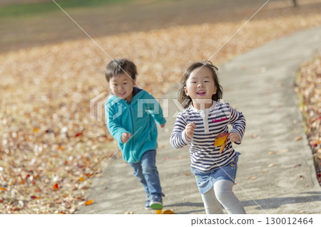 A boy and a girl playing in a park with autumn leaves 130012464