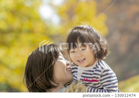 一個女孩和她的母親在被秋葉環繞的公園裡玩耍 130012474