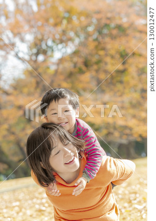 A boy and his mother playing in a park surrounded by autumn leaves 130012477