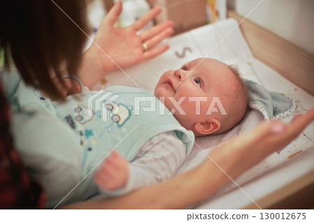 4 months old infant baby boy at changing table, mother playing with him, detail from above 4 months old infant baby boy at changing table, mother playing with him, detail from above 130012675