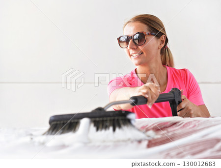 Young woman wearing pink t shirt and sunglasses cleaning her car in self service carwash 130012683