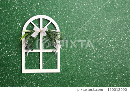 Little decorative wooden window with lace bow and flower on green stucco wall. Home sweet home style background. Charming wood window adorned with lace-trimmed bow and flower. Copy space for text 130012990