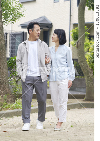 Middle-aged couple walking arm in arm outdoors, whole body Middle-aged couple walking arm in arm outdoors, whole body 130013593