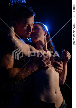 Couple embracing under cascading water with dramatic lighting at night 130014002