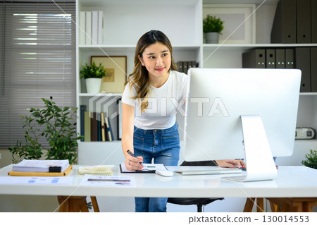 Young entrepreneur working at desktop computer and taking notes in modern office. 130014553