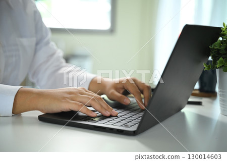 Close up of hands typing on laptop keyboard in modern office workspace 130014603