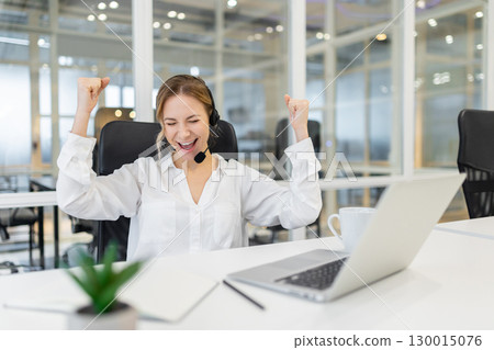 Young woman at the laptop in the office looking excited and contented 130015076