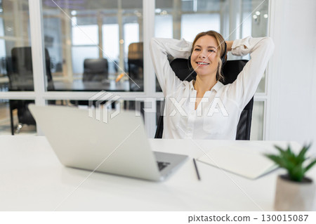 Young woman sitting in the office and stretching after a long working day 130015087