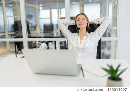 Young woman sitting in the office and stretching after a long working day Young woman sitting in the office and stretching after a long working day 130015097