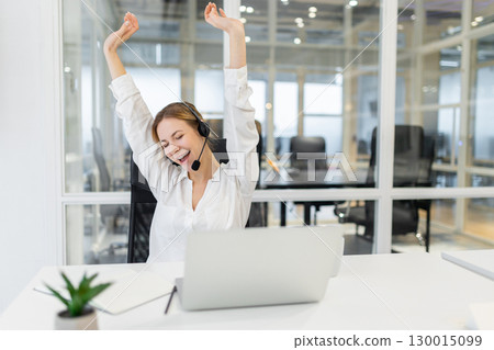 Young woman sitting in the office and stretching after a long working day 130015099