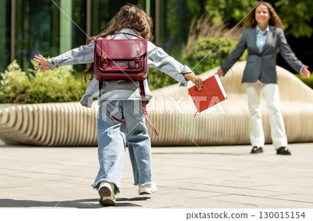 Female child joyfully running toward her mother in soft daylight 130015154