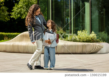 Mother in business suit standing with daughter holding documents Mother in business suit standing with daughter holding documents 130015199