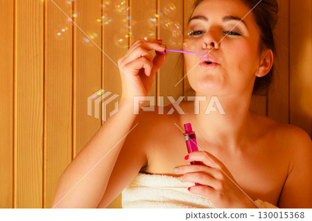 woman relaxing in sauna room blowing soap bubbles woman relaxing in sauna room blowing soap bubbles 130015368