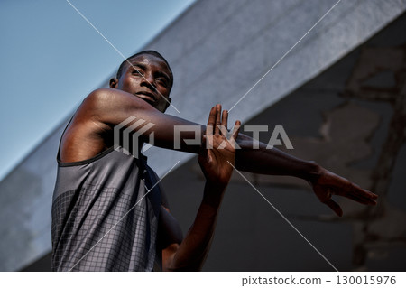 Athletic man stretching arm during outdoor workout under blue sky 130015976