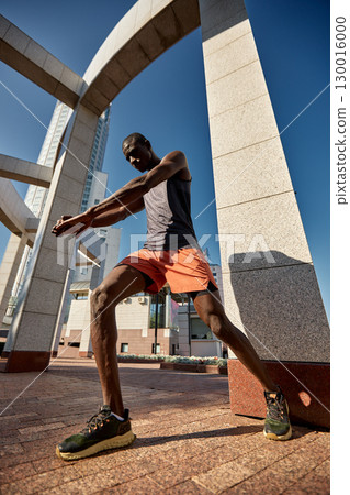 Athlete stretching outdoors under a modern architectural structure on a sunny day Athlete stretching outdoors under a modern architectural structure on a sunny day 130016000
