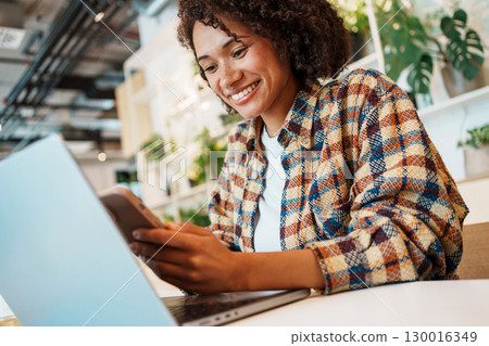 A Smiling Woman Actively Working on Her Laptop in a Cozy and Inviting Indoor Space 130016349