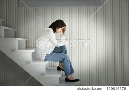 Middle-aged woman sitting on the stairs and looking down, negative Middle-aged woman sitting on the stairs and looking down, negative 130016376
