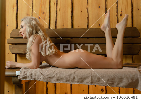 Relaxing woman enjoying tranquil sauna experience with natural wood decor 130016481