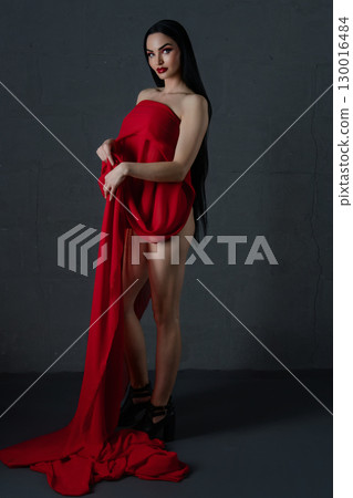 Elegant woman in stylish lingerie draped with luxurious red fabric indoors 130016484