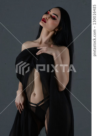 Woman poses elegantly in black lingerie with flowing fabric in a studio setting 130016485