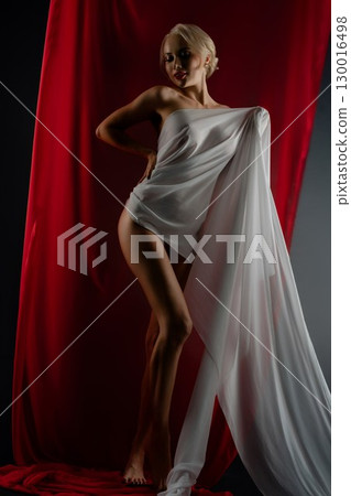 Elegant woman poses with flowing cloth in studio setting, dramatic lighting 130016498