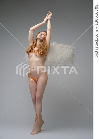 Red naked woman with angel wings showcases body art in a studio setting Red naked woman with angel wings showcases body art in a studio setting 130016509