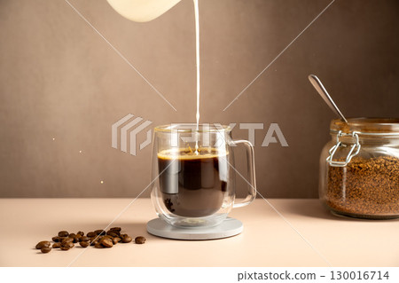 Pouring milk in a glass cup mug of coffee, instant coffee drink 130016714